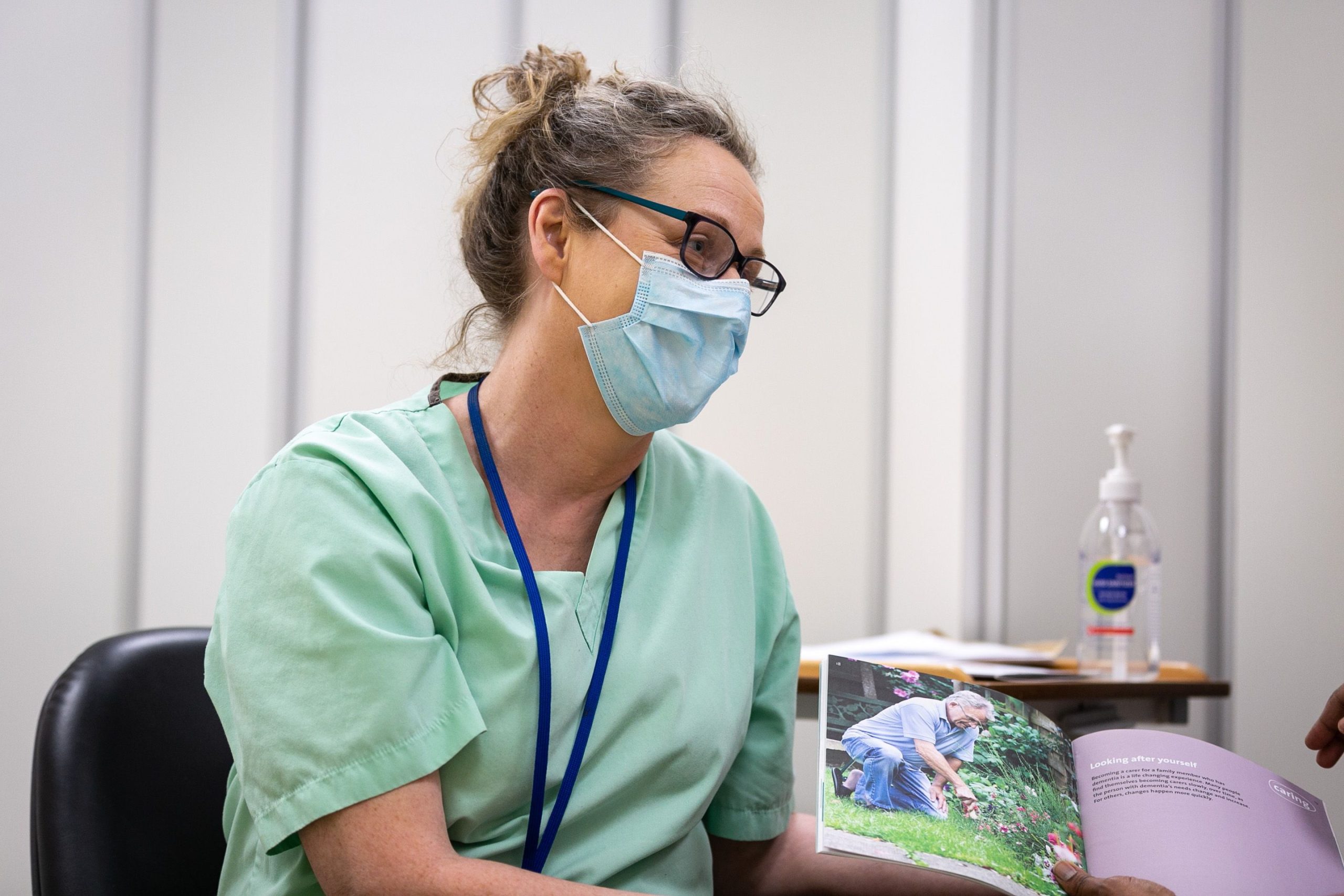 Doctor shows book to patient out of the image. They are wearing scrubs and a medical mask.